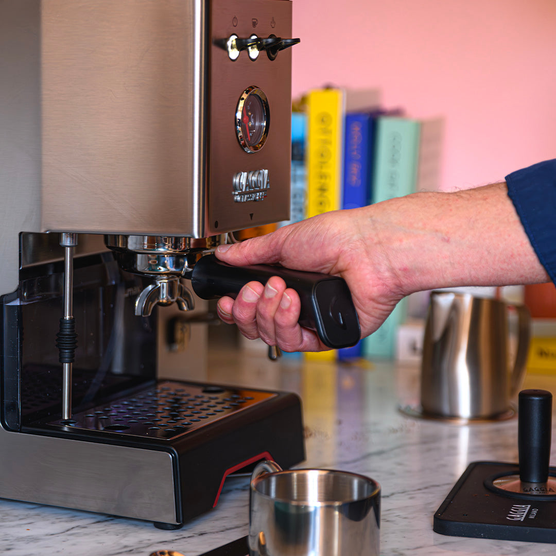 A hand locks a 58 mm portafilter into a Gaggia Classic UP Semi-Automatic Espresso Machine EG2500/00.