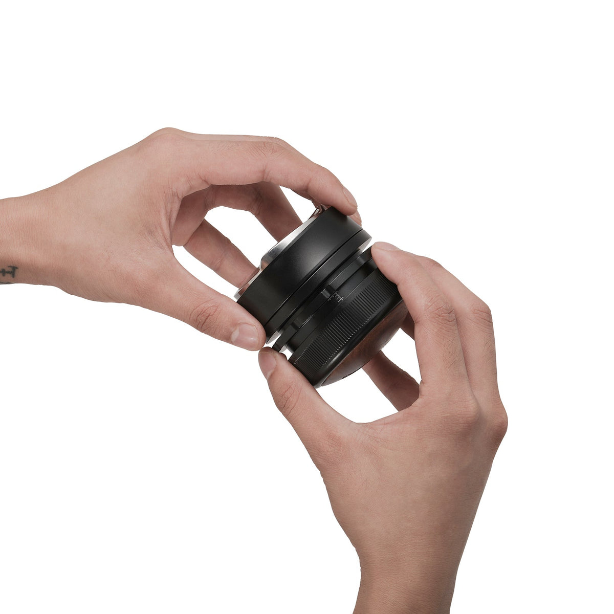 Two hands hold and adjust the MHW-3BOMBER Coffee Gravity Distributor 58.35mm, featuring a cyclone-shaped base, against a plain white background.