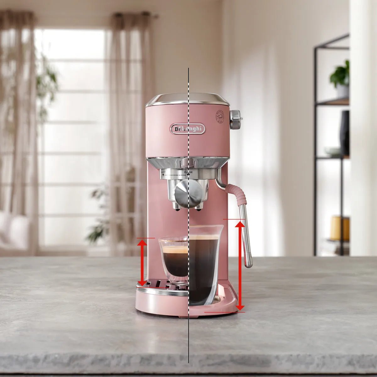 A DeLonghi Dedica Duo Espresso Machine with Cold Brew EC890PK (Rosé) sits on a kitchen counter, glass of coffee beneath the spout. Red arrows highlight cup height adjustment; shelves and a window appear softly lit in the background.