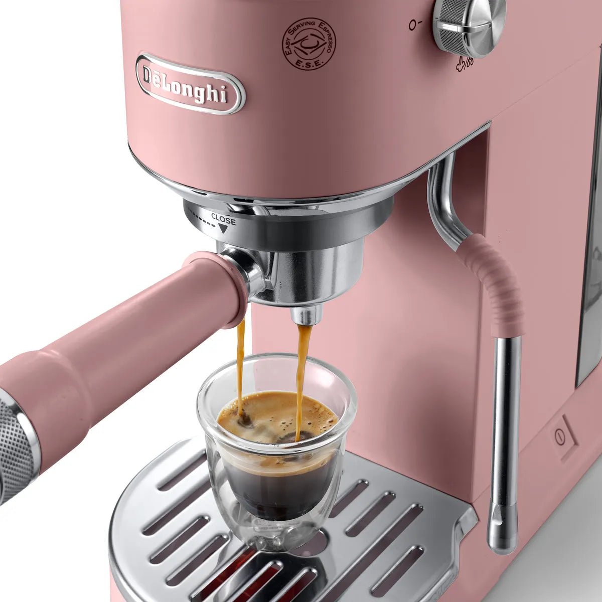 The DeLonghi Dedica Duo Espresso Machine with Cold Brew EC890PK (Rosé) brews two streams of coffee into a clear glass cup on its metallic drip tray.