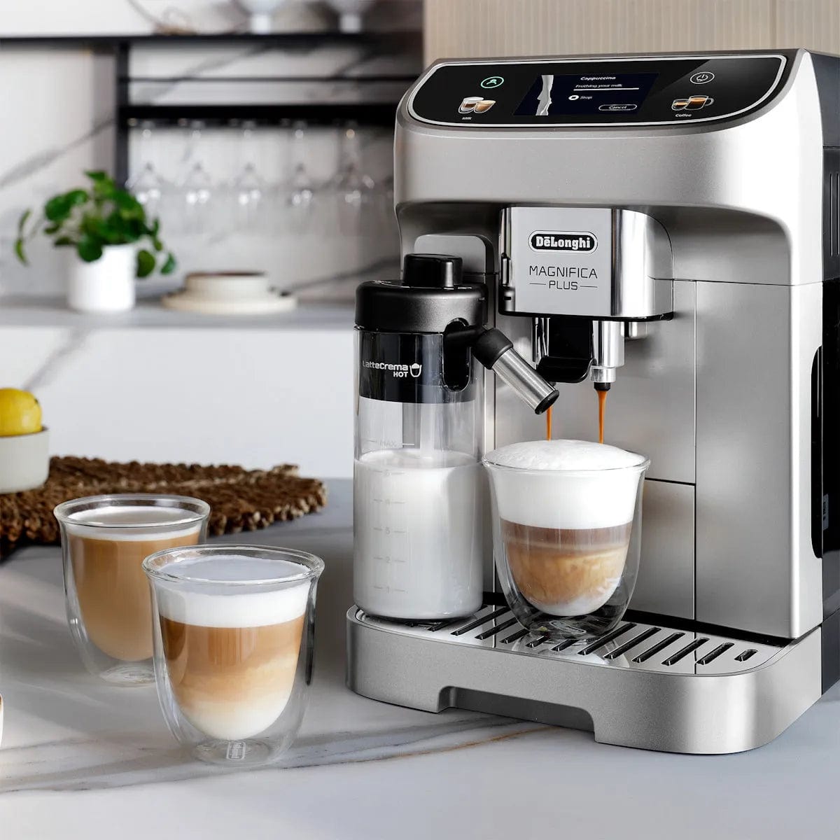 A DeLonghi Magnifica Plus Super Automatic Espresso Machine with LatteCrema System (model ECAM32070SB) brews two cappuccinos, served in double-wall glass cups on a modern kitchen counter.