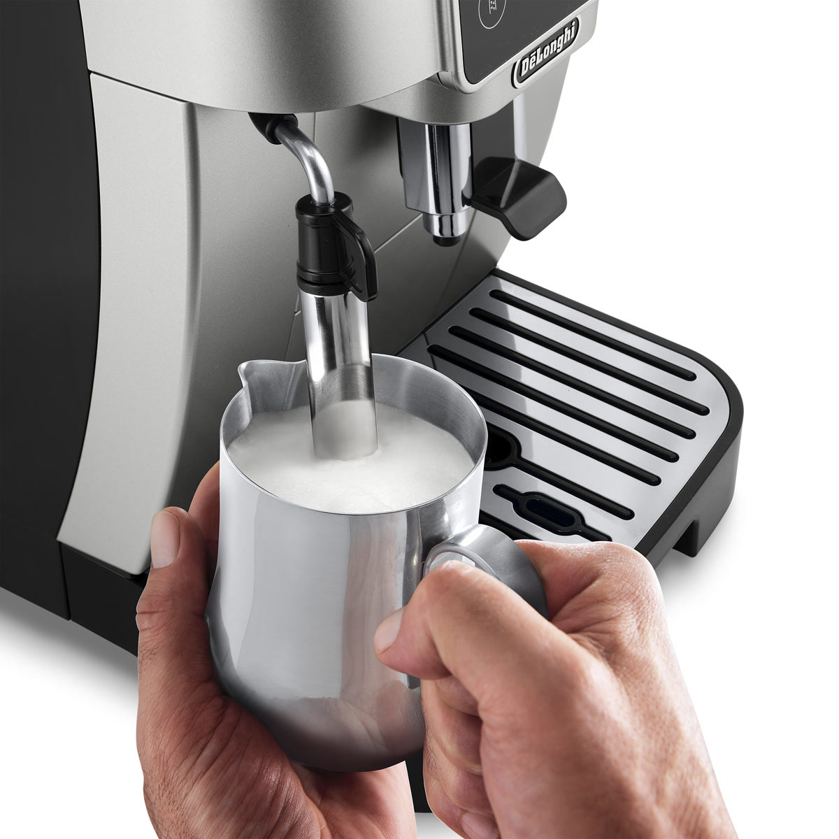 A person uses the De'Longhi Magnifica Start Super Automatic Espresso Machine ECAM22022SB (Silver) by DeLonghi, holding a metal pitcher under the steam wand to expertly froth milk.