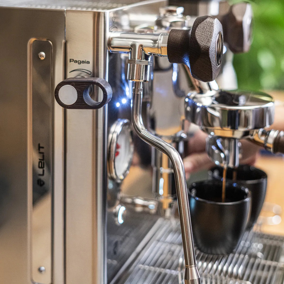 A close-up of the Lelit Mara X3 Semi-Automatic Heat-Exchange Espresso Machine PL62X3 (Stainless Steel) with wooden knobs and a steam wand, brewing coffee into a black cup. The"Lelit" brand name is clearly visible on the side.