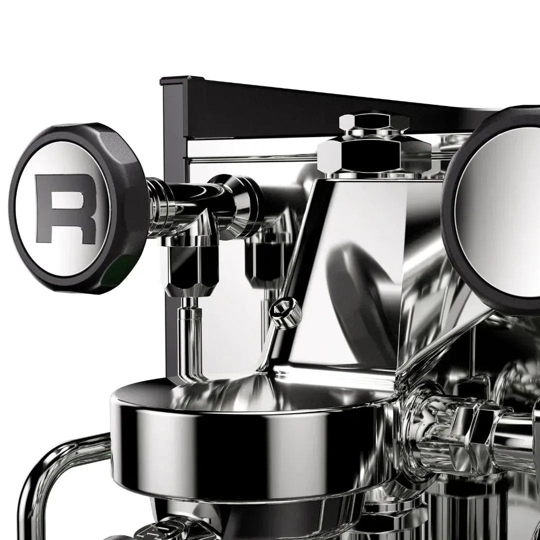 A close-up of the Rocket Appartamento TCA Espresso Machine (RE502A3B12) showcases its sleek stainless steel design with black accents. The round knobs and polished surfaces allow for precise temperature control, reflecting light off its modern, industrial look.