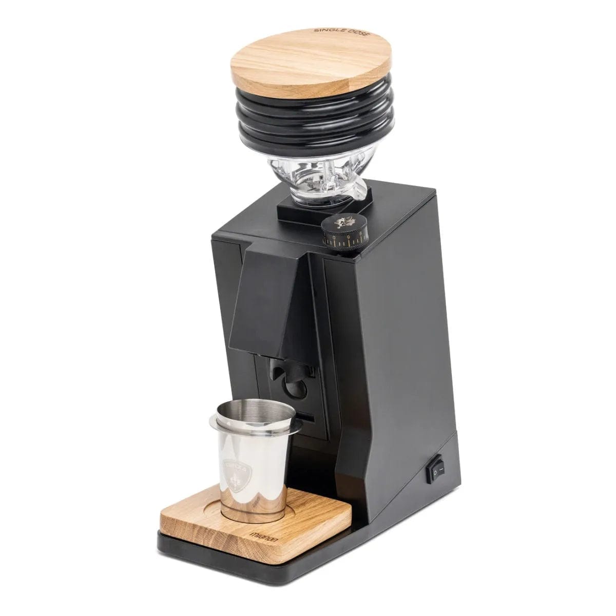 The Eureka Oro Mignon Single Dose Grinder | Inclined To Zero Retention Grinder v1.1 (Black) by Eureka is a black and wooden coffee grinder with a clear bean hopper on top. This compact grinder boasts a modern, minimalist design and features near-zero retention grinding with large flat burrs. The stainless steel dosing cup is placed on a wooden tray at the base, and a power switch is visible on the side.