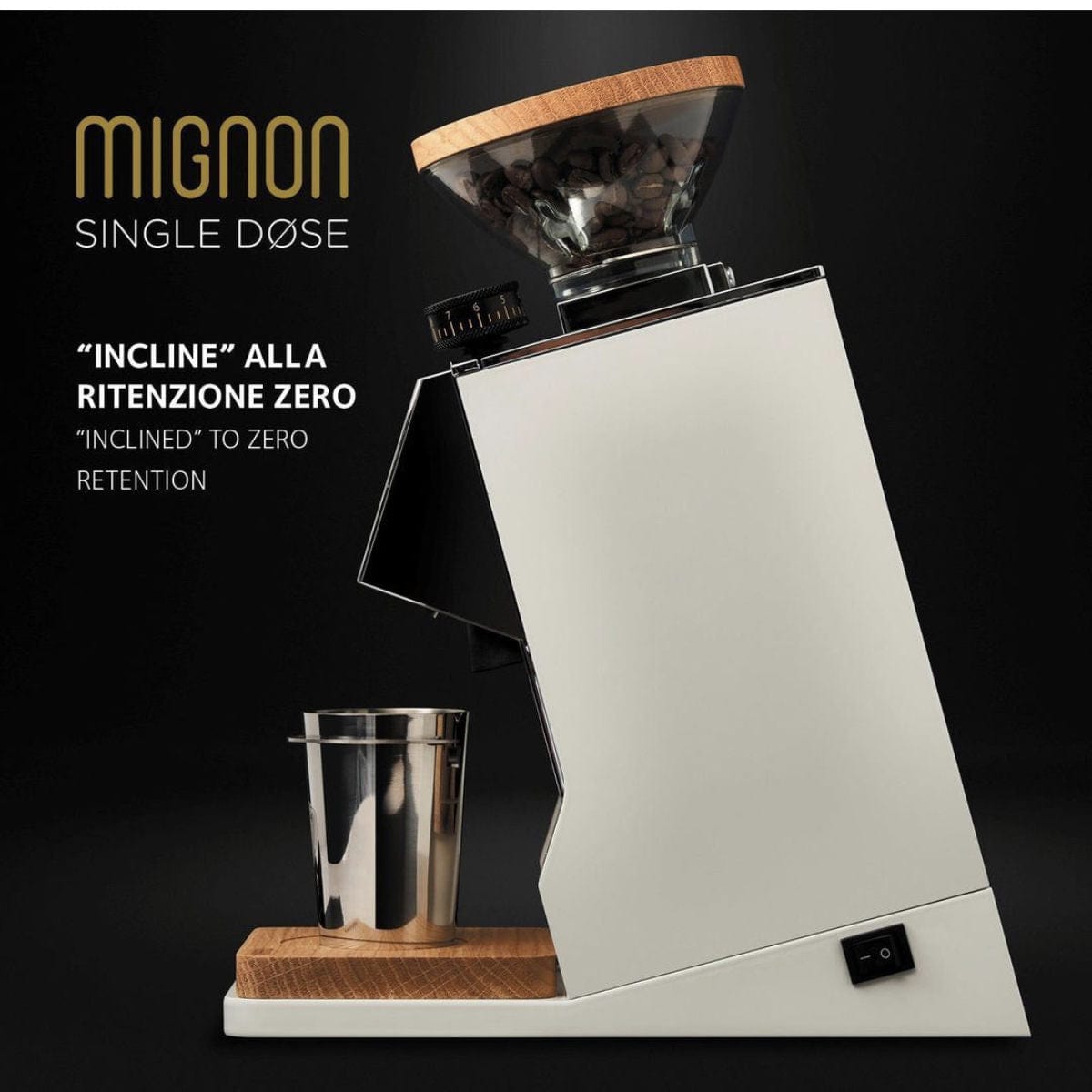 A sleek, black coffee grinder with a transparent bean hopper showcasing coffee beans. Below, a grind container is ready for use. The text on the image reads "Eureka Oro Mignon Single Dose Grinder | Inclined to Zero Retention" in English and Italian, emphasizing its near-zero retention grinding capabilities.