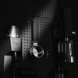 Black and white photo of coffee equipment on a perforated wall, featuring the MHW-3BOMBER YU Series Unibody Bottomless Portafilter 58mm and grinder, with dramatic lighting to highlight contrast and extraction efficiency.