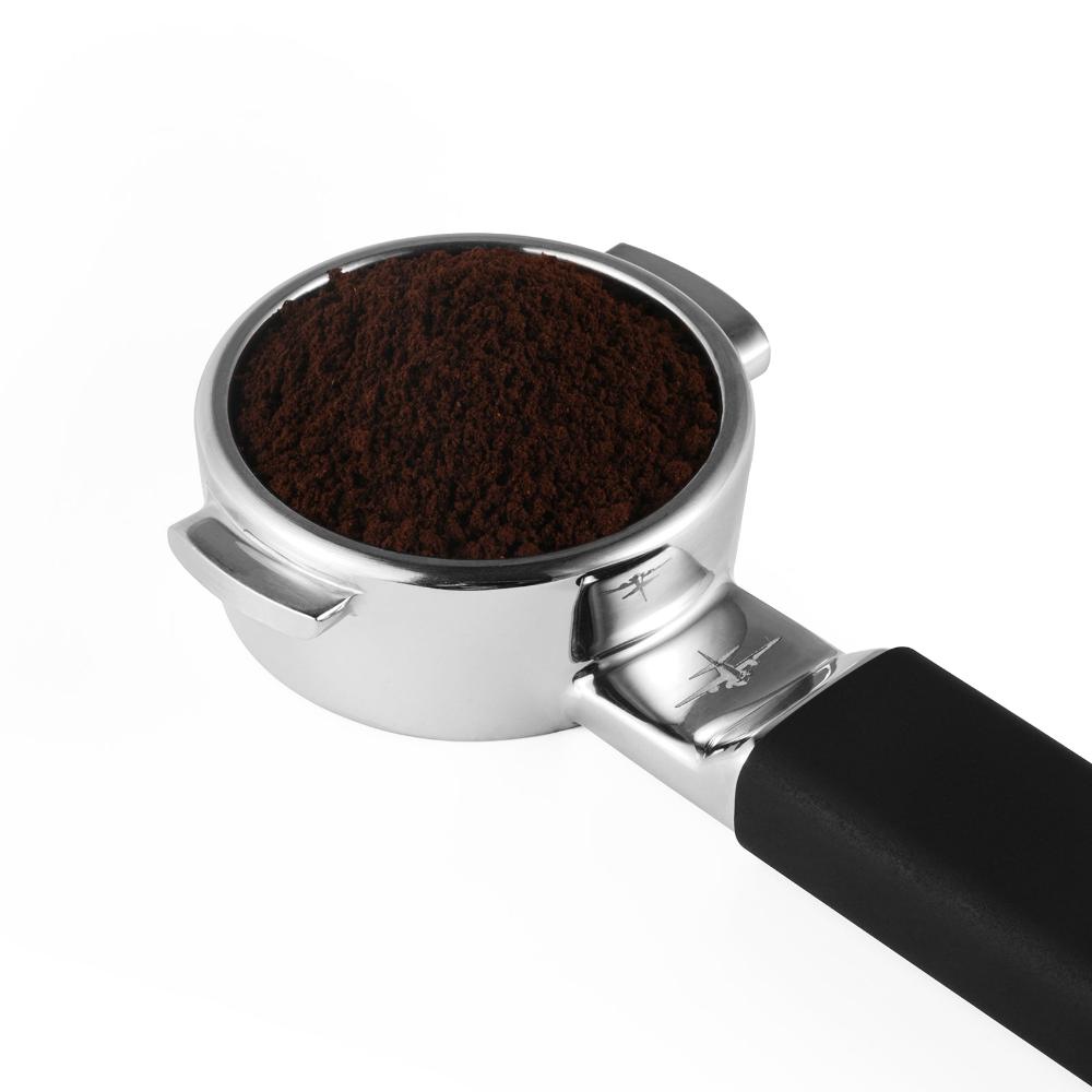 The MHW-3BOMBER YU Series Unibody Bottomless Portafilter 58mm, loaded with finely ground coffee and precision filter holes for optimal espresso extraction, is set against a white background.
