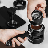 A person uses a distributor tool to level and tamp coffee grounds in the MHW-3BOMBER YU Series Unibody Bottomless Portafilter 58mm, ensuring even distribution and optimal espresso extraction.