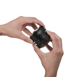 Two hands hold and adjust the MHW-3BOMBER Coffee Gravity Distributor 58.35mm, featuring a cyclone-shaped base, against a plain white background.
