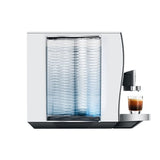 The Jura Z10 Aluminum White Super Automatic Hot Coffee & Espresso, Cold Brew, & Specialty Beverage Machine by Jura, featuring a sleek metallic design and a transparent water tank, is dispensing a shot of espresso into a small glass cup.