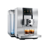 A Jura Z10 Aluminum White Super Automatic Coffee & Espresso Machine by Jura is brewing two cups of espresso, visible in the filled glasses on its drip tray. The machine features a digital display, a water tank positioned on the left side, and uses a Product Recognising Grinder to ensure perfectly ground coffee every time.