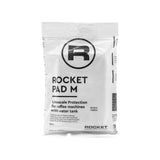 A white packet labeled "Rocket Espresso Water Softener - BMT Pad M RA92504624" featuring a large "R" logo at the top. The packet is designed for limescale reduction in coffee machines with water tanks. Text on the packet indicates it contains 100g and lists product numbers, ensuring your espresso machine stays in top condition.