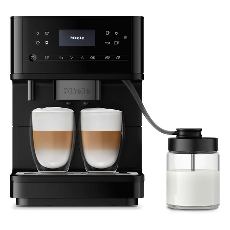 A Miele CM 6360 Super Automatic Countertop Coffee & Espresso Machine (Matte Black) by Miele stands on a plain background, with two glasses of layered cappuccinos under the spouts and a milk container attached by a tube.