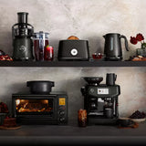 Two kitchen shelves showcase a juicer, blender, toaster, and the Breville the Smart Kettle Luxe 1.7L BKE845BTR (Black Truffle) on top. Below are a toaster oven and espresso machine, surrounded by drinks, bread, and desserts.