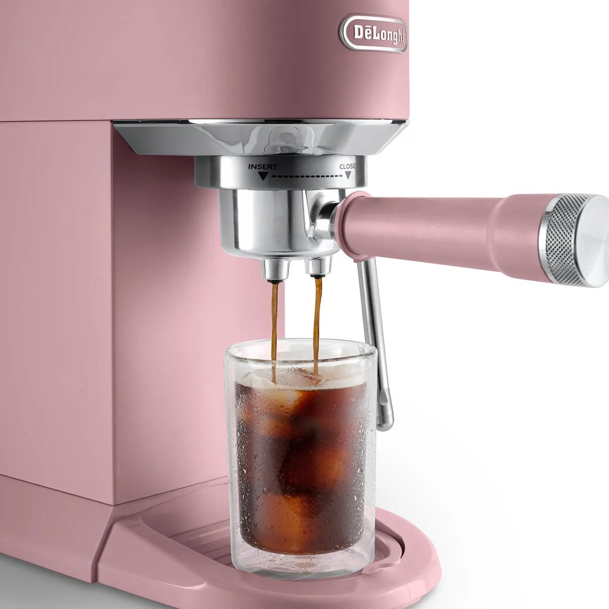 A pink DeLonghi Dedica Duo Espresso Machine with Cold Brew EC890PK (Rosé) pours coffee over ice into a clear glass on the drip tray.