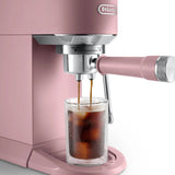 A pink DeLonghi Dedica Duo Espresso Machine with Cold Brew EC890PK (Rosé) pours coffee over ice into a clear glass on the drip tray.