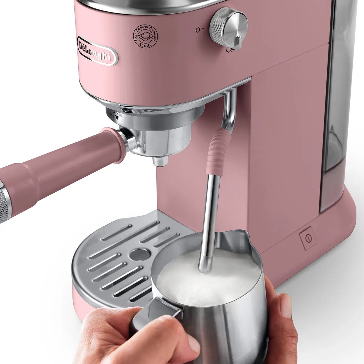 A hand holds a metal milk frothing pitcher under the steam wand of the DeLonghi Dedica Duo Espresso Machine with Cold Brew EC890PK (Rosé), using My LatteArt technology to froth milk.