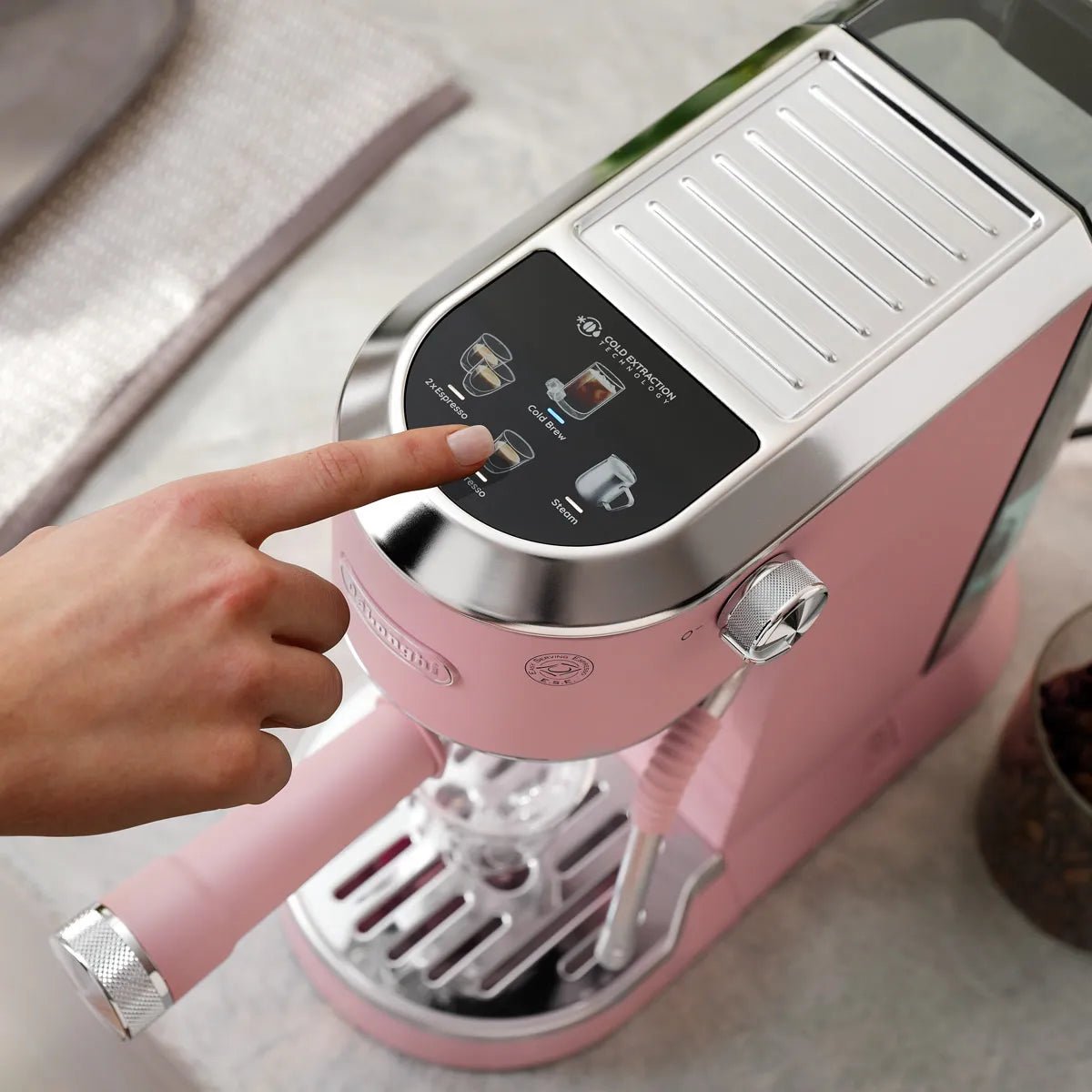A person presses a button on the compact De'Longhi Dedica Duo Espresso Machine with Cold Brew EC890PK (Rosé).