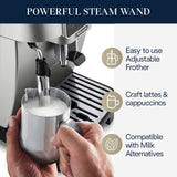 A hand froths milk with a steam wand on the De'Longhi Magnifica Start Super Automatic Espresso Machine ECAM22022SB (Silver) by DeLonghi. Three icons and text highlight its adjustable frother, LatteCrema System for crafting lattes and cappuccinos, and compatibility with milk alternatives.