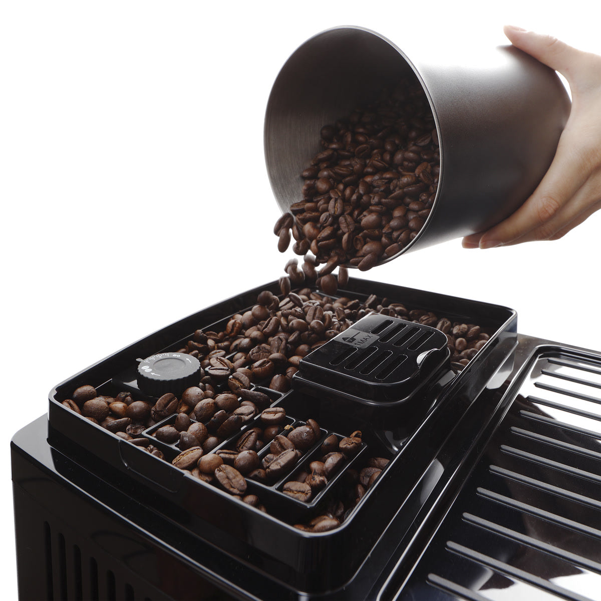 A hand pours coffee beans from a metal container into the bean compartment of the DeLonghi Magnifica Start Super Automatic Espresso Machine with LatteCrema System ECAM22080SB (Silver), which features a built-in conical burr grinder.