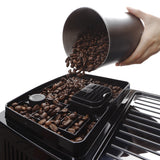 A hand pours coffee beans from a metal container into the bean hopper of a DeLonghi Magnifica Start Super Automatic Espresso Machine ECAM22022SB (Silver), preparing them for the integrated conical burr grinder.