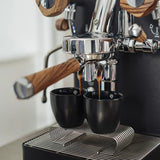 A close-up of the Lelit Mara X3 Semi-Automatic Heat-Exchange Espresso Machine PL62X3 (Black) by Lelit with wooden handles, brewing two shots of espresso into black cups on a metal drip tray.