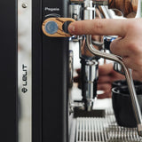 A hand presses the wooden "Pagaia" button on a Lelit Mara X3 Semi-Automatic Heat-Exchange Espresso Machine PL62X3 (Black), with its steam wand and black cups in the background.