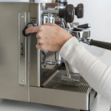 A person in a light-colored long-sleeve shirt presses a button on the stainless steel Lelit Mara X3 Semi-Automatic Heat-Exchange Espresso Machine PL62X3, with a cup placed under the portafilter.