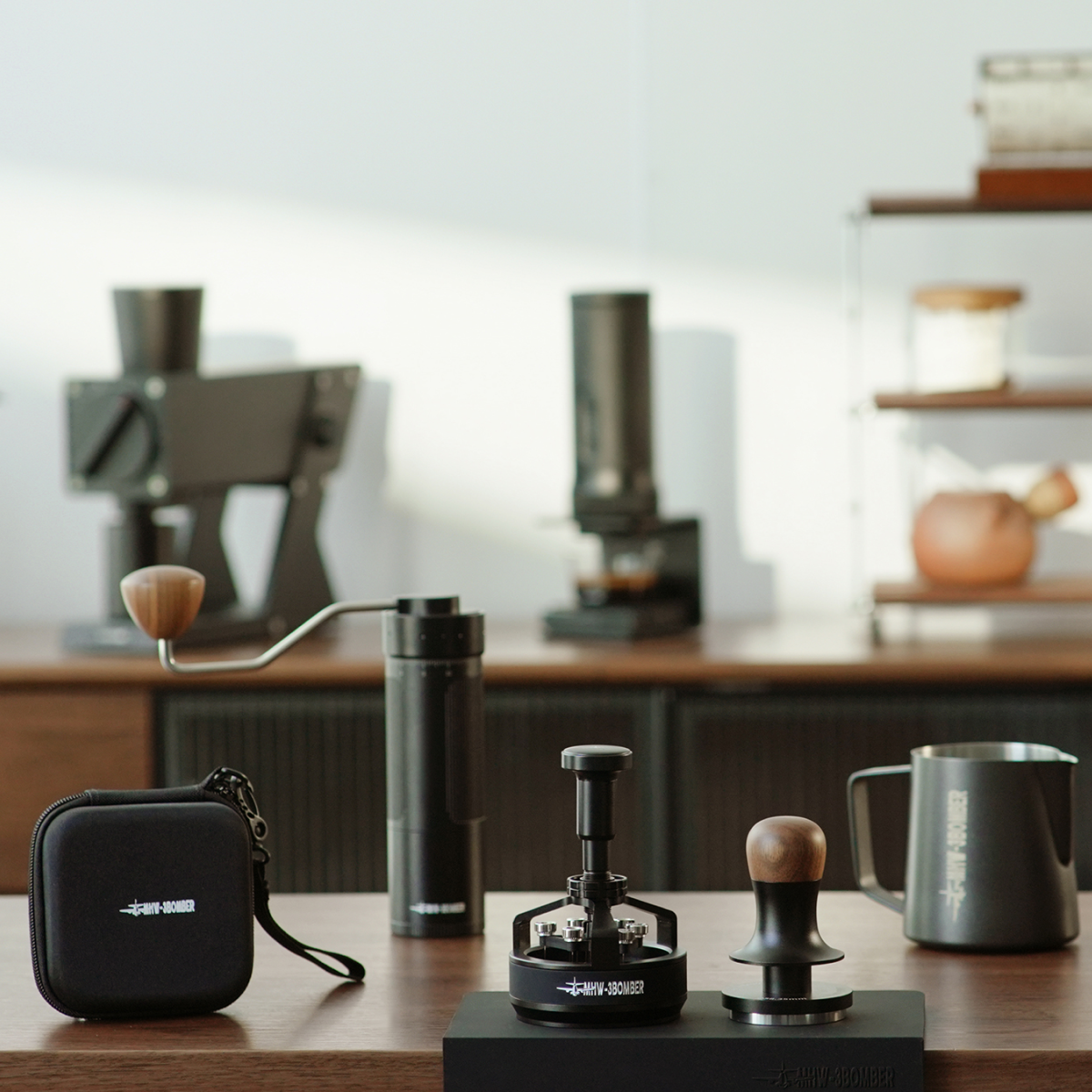 The MHW-3BOMBER Master Barista Set Bundle, featuring premium coffee tools, is showcased on a wooden counter with blurred machines and shelves in the background under warm, minimalist lighting.