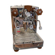 The Lelit Bianca 3 Semi-Automatic Dual-Boiler E61 Espresso Machine with PID PL162T (Version 3) - Returned (4607), crafted by Lelit, is an Italian-made stainless steel espresso machine featuring elegant wooden handles, precise pressure gauges, and a professional steam wand. This premium home coffee maker sits atop a reflective surface with its drip tray neatly positioned beneath the spout.