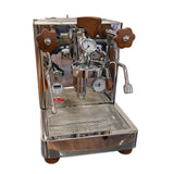 The Lelit Bianca 3 Semi-Automatic Dual-Boiler E61 Espresso Machine with PID PL162T (Version 3) - Returned (4607), crafted by Lelit, is an Italian-made stainless steel espresso machine featuring elegant wooden handles, precise pressure gauges, and a professional steam wand. This premium home coffee maker sits atop a reflective surface with its drip tray neatly positioned beneath the spout.