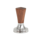The Profitec 58mm Tamper (American Walnut), featuring a combination of metal and wood, has an American walnut handle and a polished 58mm espresso tamper base with the "PROFITEC" brand name engraved on the bottom rim. It is shown against a plain white background.