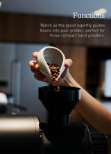 A hand pours coffee beans from the Loveramics Coffee Dosing Tray (Matte Dark Green) into a black grinder. Text above describes how the tray’s spout guides beans seamlessly into hand grinders, showcasing this Loveramics accessory favored by coffee enthusiasts like James Hoffmann. The softly blurred kitchen decor provides an inviting background.