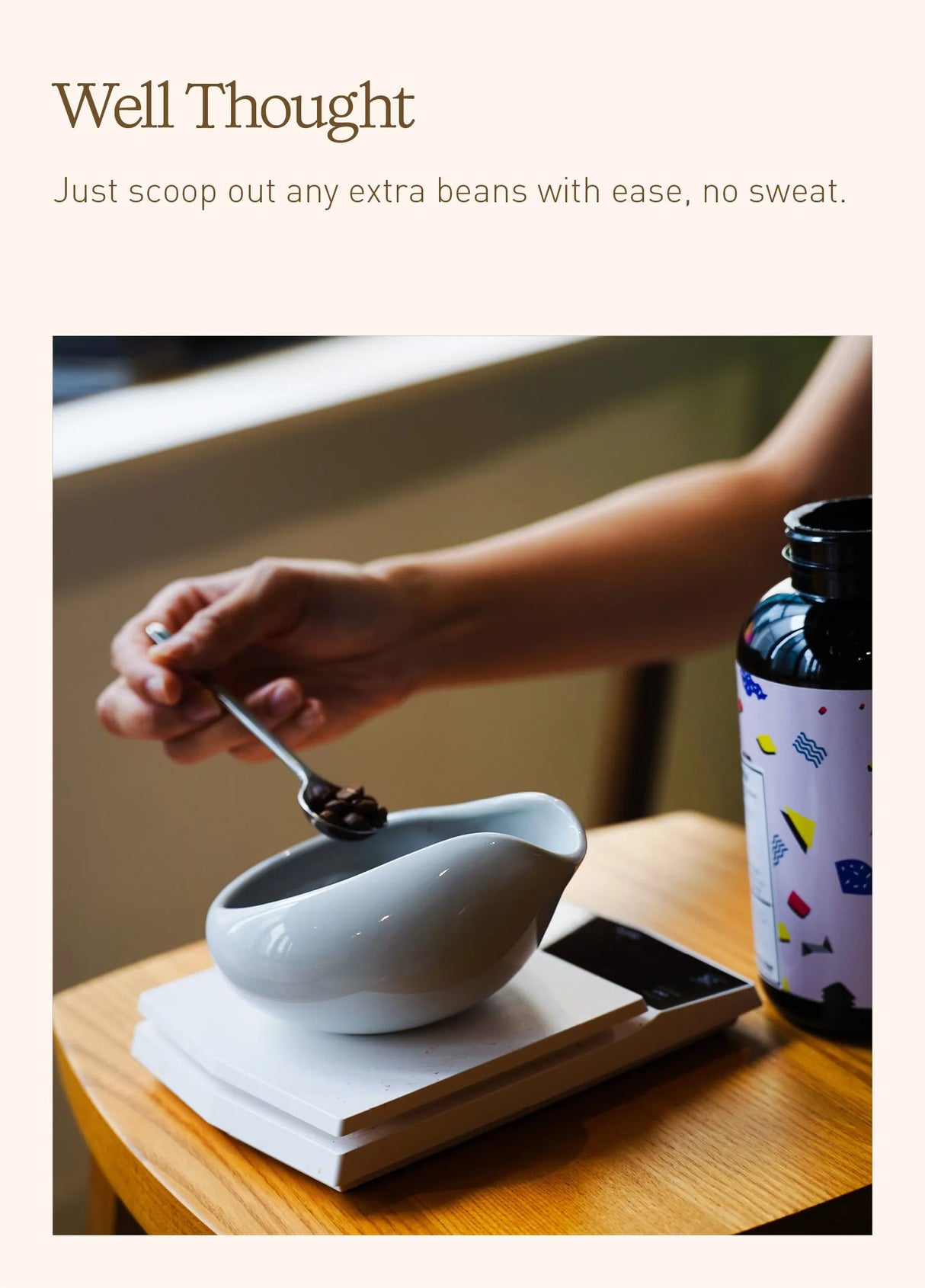 A person scoops beans from a Loveramics Coffee Dosing Tray (Matte Dark Green, Set of 2) on a digital scale, with a patterned bottle nearby on a wooden table—a setup inspired by James Hoffmann and his approach to precise coffee preparation.