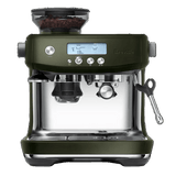 A Breville The Barista Pro Espresso Machine BES878OLT in Olive Tapenade, featuring a digital display with icons and numbers, two espresso spouts, a built-in grinder on top filled with coffee beans, and a steam wand on the right side. This machine includes the ThermoJet heating system and various buttons for settings.