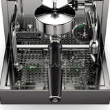 The image showcases a Rocket Appartamento TCA Espresso Machine with Flow Control RE502A3B12 in Stainless Steel - Black, highlighting the portafilter handle, pressure gauge, and stainless steel details against the perforated drip tray. As a premium home espresso maker, it features sleek design and precise temperature control.