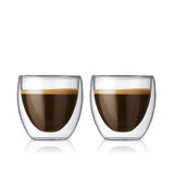 Two sleek Bodum Pavina Small 2.5oz Double Walled Coffee & Espresso Glasses, each filled with dark espresso topped with a thin layer of crema, sit side by side on a plain white background. The thermo insulated borosilicate glass keeps your coffee hot while the exterior stays cool to touch.