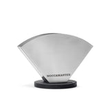 The Technivorm Moccamaster Stainless Steel Coffee Filter Holder MA003 features a sleek design with the "Moccamaster" brand name engraved on the front. It sits on a round black base and is shaped like a coffee filter cone, keeping your filters organized and easily accessible. For added convenience, it can be mounted anywhere in your kitchen using 3M tape.