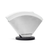 The Technivorm Moccamaster Stainless Steel Coffee Filter Holder MA003 by Moccamaster is shown. This filter holder features a sleek, silver design with rounded edges and rests on a black base. The brand name "MOCCAMASTER" is printed in black at the bottom front, making your cone-shaped filters easily accessible.