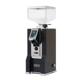 A matte black Eureka Oro Mignon Stark grinder with a clear hopper on top, featuring a digital display and control buttons on the front. The brand name "Eureka" is visible at the bottom, and it boasts 65 mm flat burrs along with an ACE Anti-clump system for optimal performance.