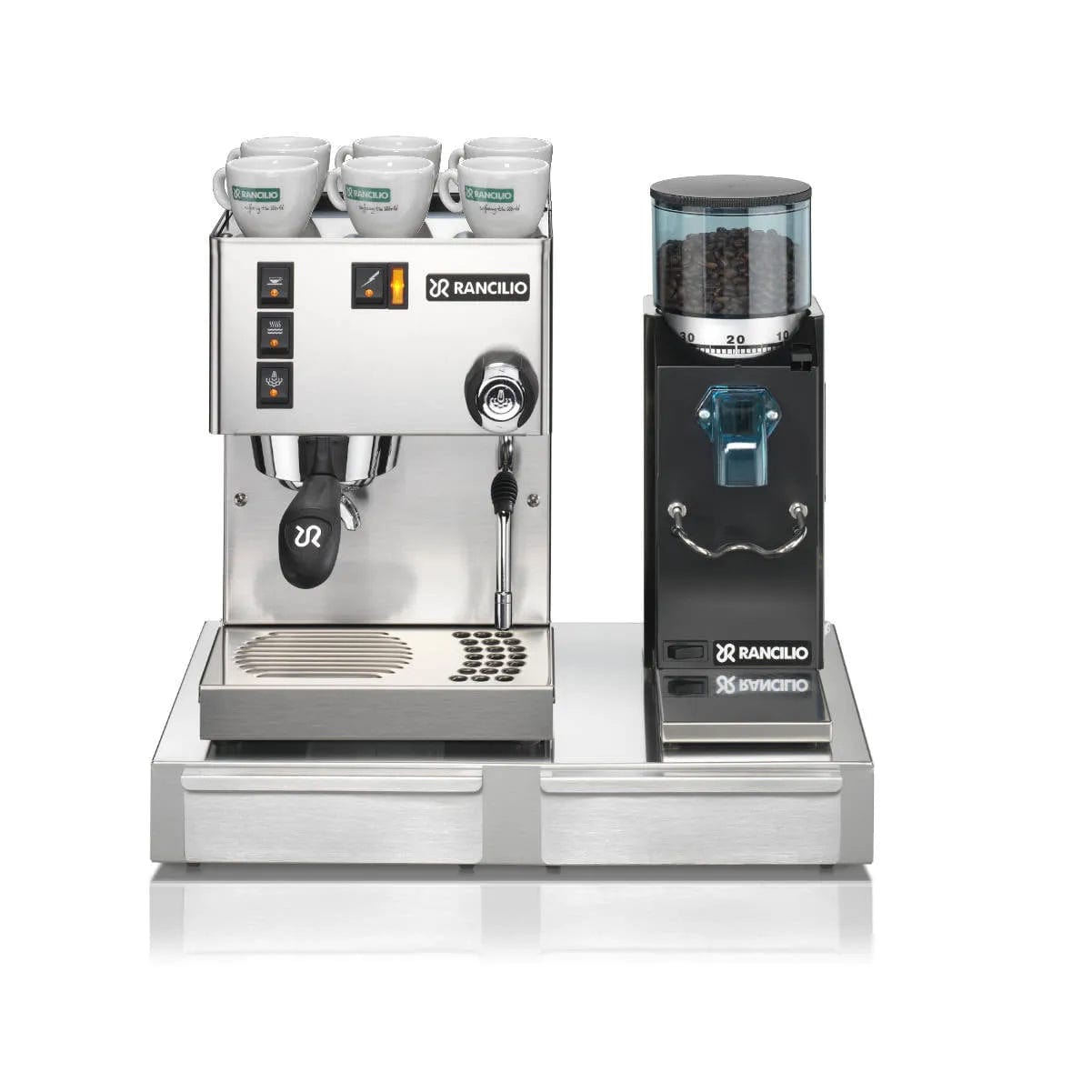 A Rancilio Silvia espresso machine and Rocky Grinder set sit atop a stainless steel Rancilio Base BS 50. The espresso machine features four control buttons, a steam wand, and three espresso cups placed on top. The coffee grinder, filled with coffee beans, comes with a front dispenser for easy access.