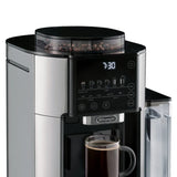 The DeLonghi TrueBrew Fully Automatic Drip Coffee Machine CAM51035M in stainless steel with a thermal carafe features a digital display showing 7:30. The control panel includes buttons for various coffee types and strength settings. A transparent water reservoir is on the right side, and a mug of single-serve drip coffee is positioned beneath the dispenser.